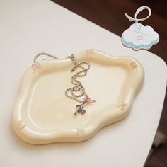 a white tray with a necklace on it sitting on a table next to a baby pacifier