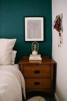 a bed room with a neatly made bed next to a green wall and a wooden night stand