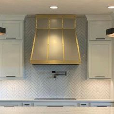 a kitchen with white cabinets and gold hood