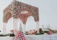 an outdoor wedding setup with pink and white flowers hanging from it's ceiling,