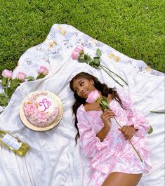 a woman laying on the grass with a cake and flowers in her hand next to it