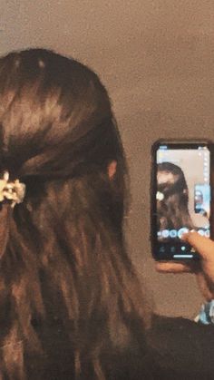 a woman with long hair is taking a photo on her cell phone while wearing a flower in her hair