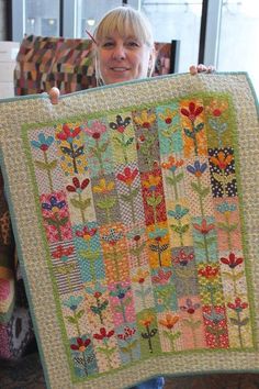 a woman holding up a quilt made with flowers