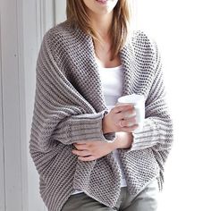 a woman sitting on a window sill with her arms crossed and holding a coffee cup