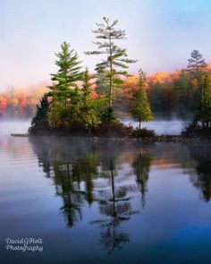 an island in the middle of a body of water surrounded by trees with autumn foliage