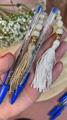 three pens with tassels and beads on them in a person's hand