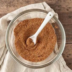 a glass bowl filled with spices on top of a wooden table next to a white napkin