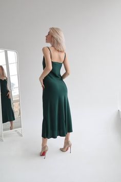 a woman standing in front of a mirror wearing a green dress and high heel shoes