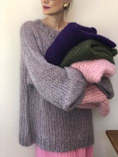 a woman is holding several sweaters in her arms and looking off to the side