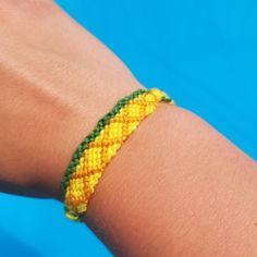 a person wearing a yellow and green beaded bracelet on their arm with a blue background