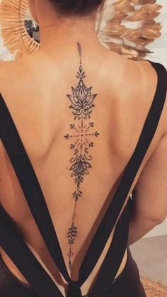 the back of a woman's neck with an intricate tattoo design on her lower back