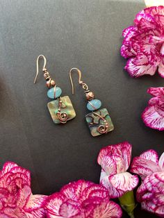 two pieces of jewelry sitting next to pink flowers