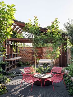 an outdoor dining area with red chairs and a round table surrounded by greenery in the foreground