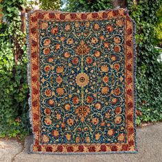 an antique persian rug is displayed in front of a tree and shrubbery on the sidewalk