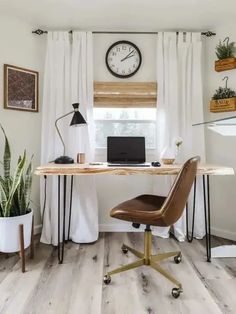 a desk with a laptop on it in front of a window and a clock mounted to the wall