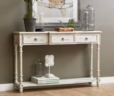 a white console table with drawers and plants on top, in front of a gray wall