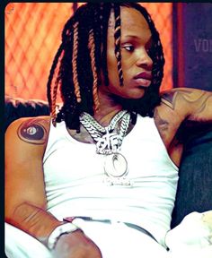 a woman with dreadlocks sitting on a couch wearing a white tank top and black pants