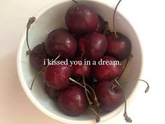 a white bowl filled with red cherries on top of a table next to an inscription that reads, i kissed you in a dream