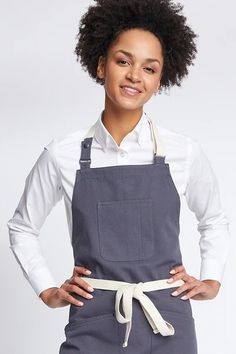 a woman wearing an apron and smiling at the camera with her hands on her hips