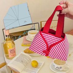 a person holding a red and white bag on top of a table next to a book