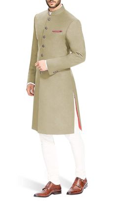 a man in a beige sherwa with white pants and brown shoes standing up