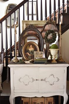 a white dresser with pictures and other items on it next to a stair case in a house