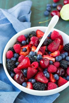 a white bowl filled with berries and kiwis on top of a blue cloth