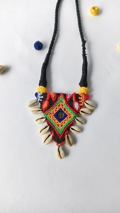 This eye-catching necklace is a celebration of tribal art and vibrant colors. It features a unique triangular pendant adorned with intricate embroidery, mirror work, and colorful threadwork. The pendant is further embellished with natural seashells, adding a touch of coastal charm. The necklace is suspended from a black braided cord, completing the bohemian aesthetic. This one-of-a-kind piece is perfect for adding a touch of global flair to any outfit. It's lightweight and comfortable to wear, m Embroidery Mirror Work, Embroidery Mirror, Bohemian Aesthetic, Coastal Charm, Intricate Embroidery, The Bohemian, Mirror Work, Handmade Necklace, Embroidery Thread