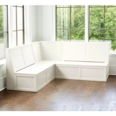 a white bench sitting in front of a window next to a wooden floor and windows