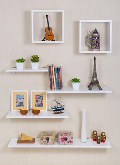 three white shelves with books, vases and other items on them against a wall