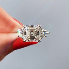 a woman's hand holding an engagement ring with three stone diamonds on the side