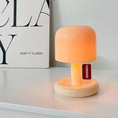 an orange lamp sitting on top of a white table next to a sign that says, keep it classy