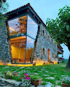 a house made out of stone and glass sitting on top of a lush green field