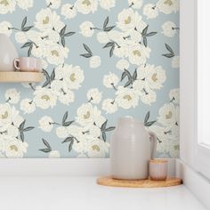 there is a vase and two cups on the shelf in front of this floral wallpaper