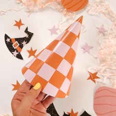 a hand holding a paper party hat on top of a white and orange checkered table cloth