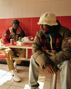 two men sitting at a table in a room with red and white tiles on the walls