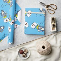 there is a blue wrapping paper with sheeps on it next to scissors and yarn