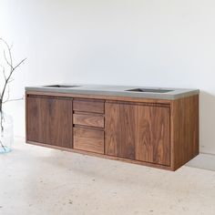 a wooden cabinet with two sinks in it and a vase on the floor next to it