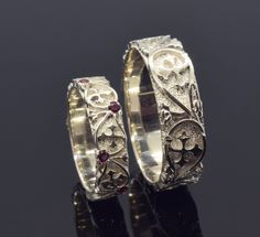 two wedding bands with skulls and flowers on them, one has red stones in the middle