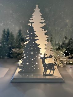 a lighted christmas tree with a deer in the middle and snow falling down on it