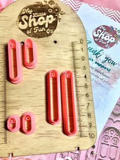 some pink plastic clips on top of a wooden cutting board next to a measuring ruler