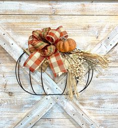 a wreath with pumpkins and wheat on it hanging from the side of a wooden wall