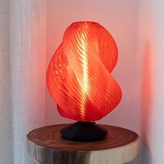 an orange lamp sitting on top of a wooden table next to a white curtained wall