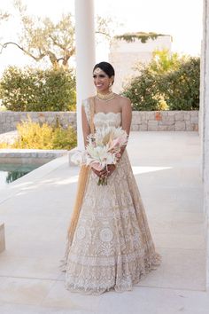 a woman standing in front of a pool wearing a wedding dress and holding a bouquet