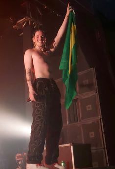 a shirtless man holding up a green and yellow flag on top of a stage