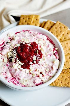 a white plate topped with a bowl of food next to crackers and a napkin