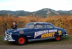 an old fashioned car is parked in front of some vines