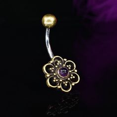 a gold flower belly ring with an amethorate stone in the center on a black background