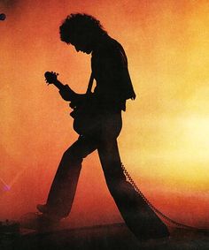 the silhouette of a man playing an electric guitar in front of a bright orange sky