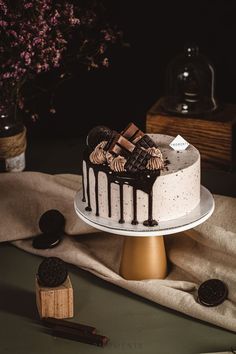 a white cake with chocolate drizzles and cookies on top sitting on a table